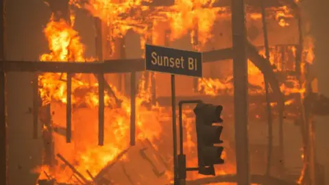 Getty Images Sebuah api yang sengit terbakar di belakang tanda jalan untuk Sunset Boulevard, selama kebakaran Los Angeles pada Januari 2025 