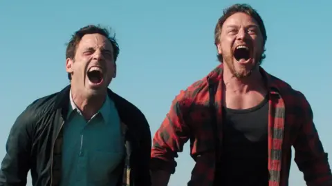 Universal Scoot McNairy's Ben (left) cathartically screams on a hilltop with James McAvoy's Paddy (right)