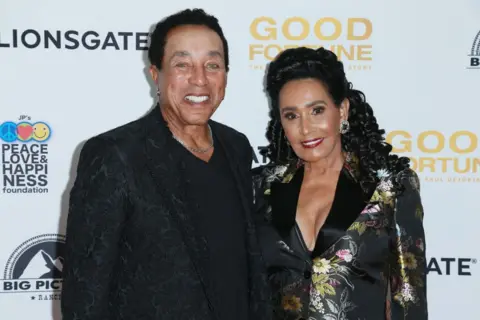 Getty Images Smokey Robinson smiles and poses for the camera with his wife, Frances, on the red carpet of a film premiere.