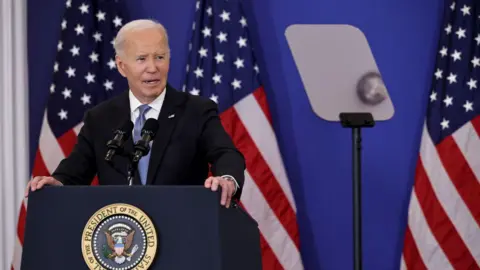 Joe Biden speaks at a lectern in front of two US flags