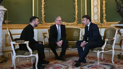 EPA Volodymyr Zelensky, Sir Kir Stmper and Emmanuel Macron are sitting on white and green chairs in a white and green panel room with gold expansion.