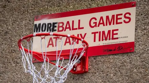 A No Ball Games sign has been changed into a basketball hoop with the words "More ball games at any time"