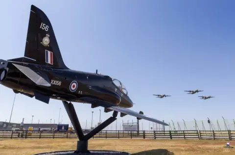 RAF Valley  Three Hercules flying over a black Hawk aircraft on the ground at RAF Valley