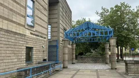 The entrance to Wolverhampton Crown Court. A blue metal frame is above the main door, with blue railings to the left of the shot.