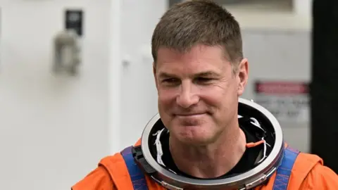 Jeremy Hansen smiles as he wears his orange and blue space suit