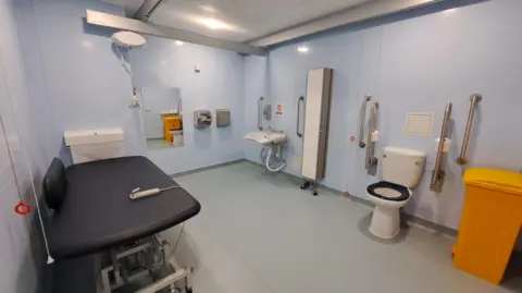 a large disabled toilet cubicle including a changing bed and hoist