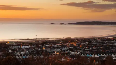 An aerial view of Swansea taken from Townhill, showing rows of terraced houses in front of Swansea Bay, taken at sunset