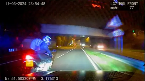 Motorcyclist looks back at police car during chase