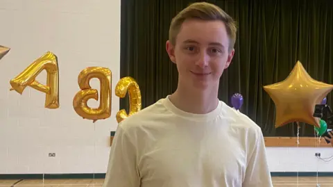 Tom wearing a white t-shirt with A, B, C balloons plus a star balloon in the background 