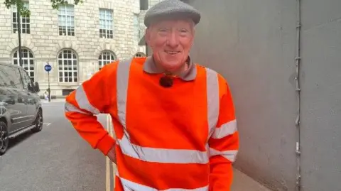 Archie Workman in a flat cap and hi-viz overalls near Manchester Central Library