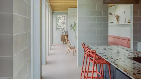 Lorenzo Zandri / RIBA A room with pastel pink coloured charis and grey walls. A speckled counter top is also set in the right of frame.