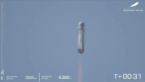 A rocket flies upwards with fire coming from its base in front of blue sky.