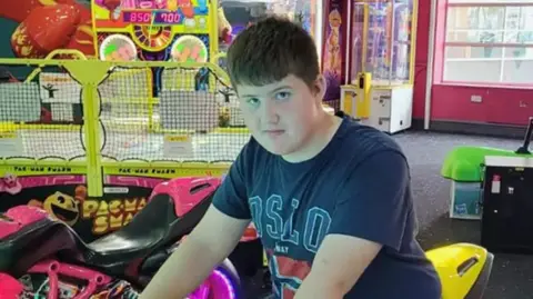 Callum Rycroft, who had short brown hair and brown eyes, sits on a motorbike ride in an amusement arcade.