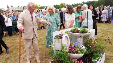 Reuters King Charles points to a toilet and sink which have been planted with flowers.