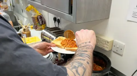 Jason Williamson scooping beans on to a plate of toast.