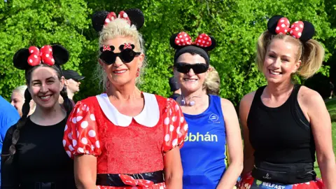 Pacemaker Four women standing next to each other. From left to right the first has plaited long brown hair, black top and is wearing Minnie Mouse ears. Next to her is Elaine who has blonde hair tied back wearing a red Minnie Mouse costume. Next to her is a lady with black clothing and short blonde hair wearing Minnie Mouse ears, and beside her is a lady with a blue top, red shorts black sunglasses and Minnie Mouse ears with her dark hair tied up.