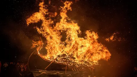 PA Media The burning long ship. Orange flames are leaping into the air