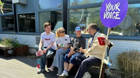 Left to right Samuel Wheatley, 21, Caitlin Noyce, 21, Taylor Jordan, 20, who are all graphics students are interviewed by BBC South East tody reporter, Peter Whittlsea. He holds a Your Voice sign.