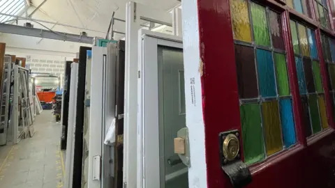 Helen Mulroy/BBC Different coloured doors are lined up behind each other in a room. The door at the front has multi-coloured stained windows.