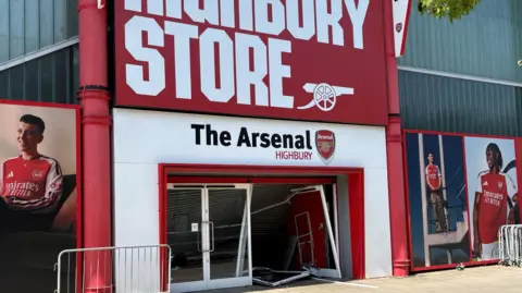 An external view of the store, with red and white signage, and large glass doors visibly damaged