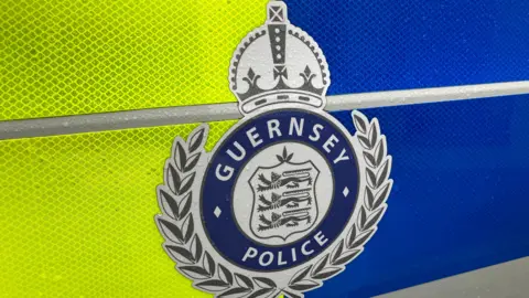 Jack Silver/BBC The Guernsey Police logo of three lions on a coat of arms, surrounded by a laurel wreath and topped by a crown, with the word Guernsey Police around it is posted over a fluorescent green and blue background in a close up of the side of a police car.