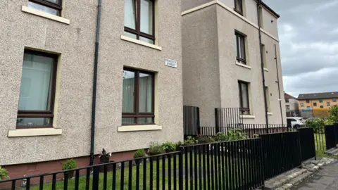 Street view of pebble-dash flats behind a black iron fence