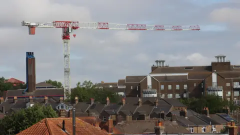 A large red and white crane rises high above the brown brick buildings below.