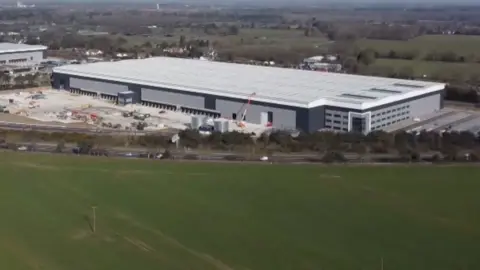 An aerial drone shot showing a giant grey warehouse under construction