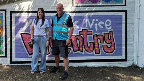 A woman and a man standing by a large mural 