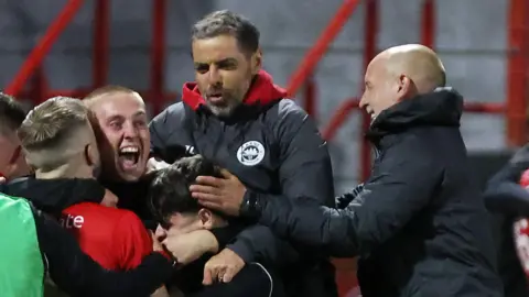 Larne manager Tiernan Lynch joins his players and staff in celebrating after the game