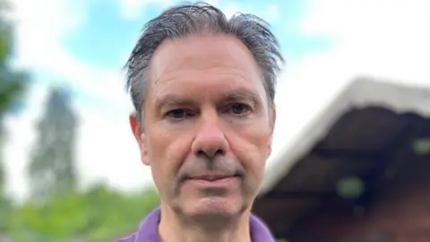 BBC Paul Harrison has grey hair combed back and is wearing a purple T-shirt 