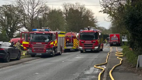 Two fire engines parked on a road. There are cars and hoses surrounding them.