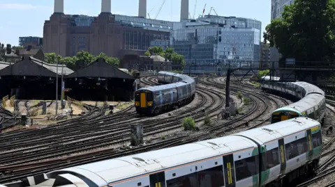 Two green Southern trains and one blue Southeastern train are seen with Battersea Power Station behind on the approach to London Victoria station