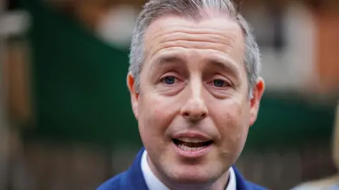 PA Media Paul Givan is speaking as he looks into the camera. It is a close up shot of his face. His mouth is open and he has short, grey hair.
