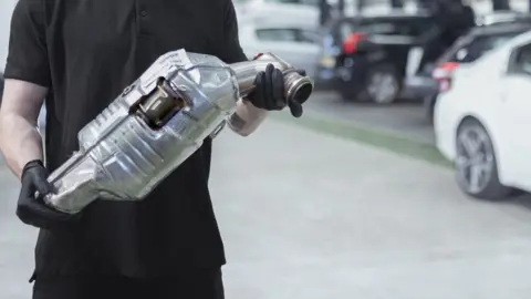 Getty The torso of a man in black holding a silver-coloured catalytic converter