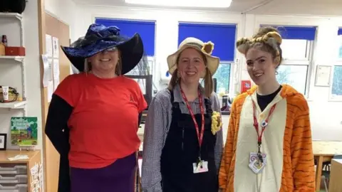 Norton Fitzwarren Primacy Three female teachers stand in a line for World Book Day, one dressed as a tiger and the other two wearing large hats
