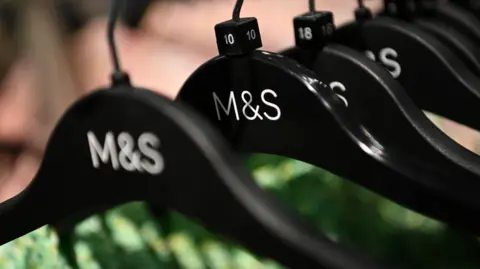 A closeup image of a row of seven black clothes hangers featuring a white M&S logo. 