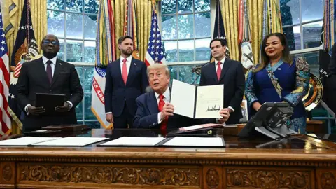 President Donald Trump holds a letter addressed to Congolese President Félix Tshisekedi congratulating him on the peace agreement with Rwanda during a meeting with Democratic Republic of the Congo Foreign Minister Thérèse Kayikwamba Wagner (R) and Rwandan Foreign Minister Olivier Nduhungirehe (L) in the Oval Office of the White House in Washington, DC, on June 27, 2025