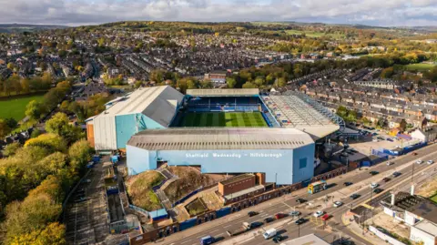 PA Media Aerial shot of Hillsborough Park, the home of Sheffield Wednesday. Surrounding hills can be seen in the distance. The stadium is surrounded by terraced houses.