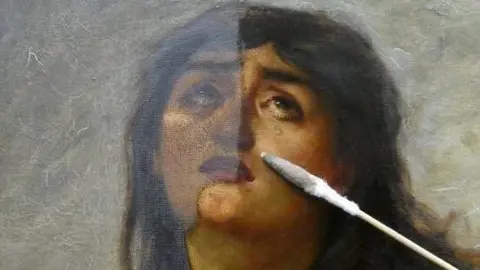 Egan, Matthews & Rose, 2025 A close up of the painting showing a woman's face. She looks to be stricken by grief and her eyes are looking upwards and she has tears on her cheeks. A conservator's brush-like tool lies on a restored section of the painting.