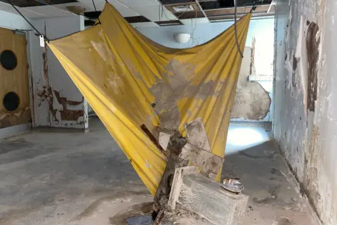 A yellow piece of material is painted to catch dust and flood water inside an abandoned hospital building