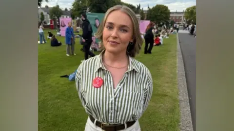 A woman with light hair and wearing a green and white shirt