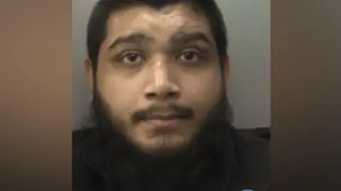 West Midlands Police A police custody photo of a man who has dark hair and a beard. he is looking directly at the camera. 