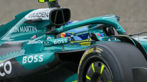 Getty Images Close up of an Aston Martin Aramco F1 car with green livery and advertising, protective bars and within it, the helmet of a driver