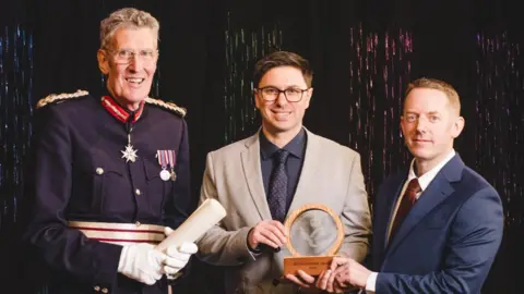 Left to right David Fursdon, His Majesty’s Lord-Lieutenant of Devon, Luminous founders Edwin Samkin and Mike Badley at the awards. The co-founders are holding a trophy. 