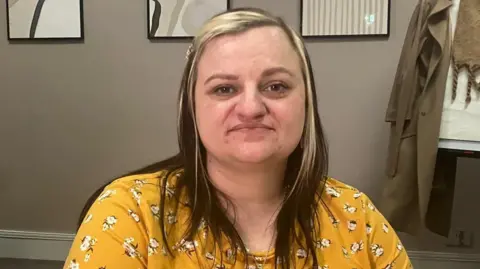 Sarah wearing a bright yellow t-shirt with a white flower print and medium brown hair with blond highlights at the front. 