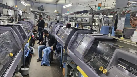 A foto de Nitin Goel mostra que dois homens operam a máquina de tricô na fábrica de roupas de cônsul em Ludhiana City, a noroeste da Índia. 