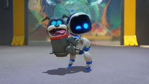 Sony A cute cartoon robot character with a black screen for a face and bright blue dots for eyes looks over his shoulder and winks at the viewer. On this back, a robotic bulldog with a blocky body and similar bright blue eyes clings on, tongue hanging out. It's a cheeky, fun scene.