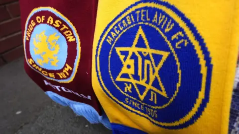 PA Media Two scarfs pictured close up - one is the claret and blue colours of Aston Villa with the Villa emblem and the words 'Pride of Aston', the second is yellow and blue, with the Maccabi Tel Aviv crest. 