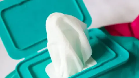 A green packet of wet wipes with one wipe coming out.
